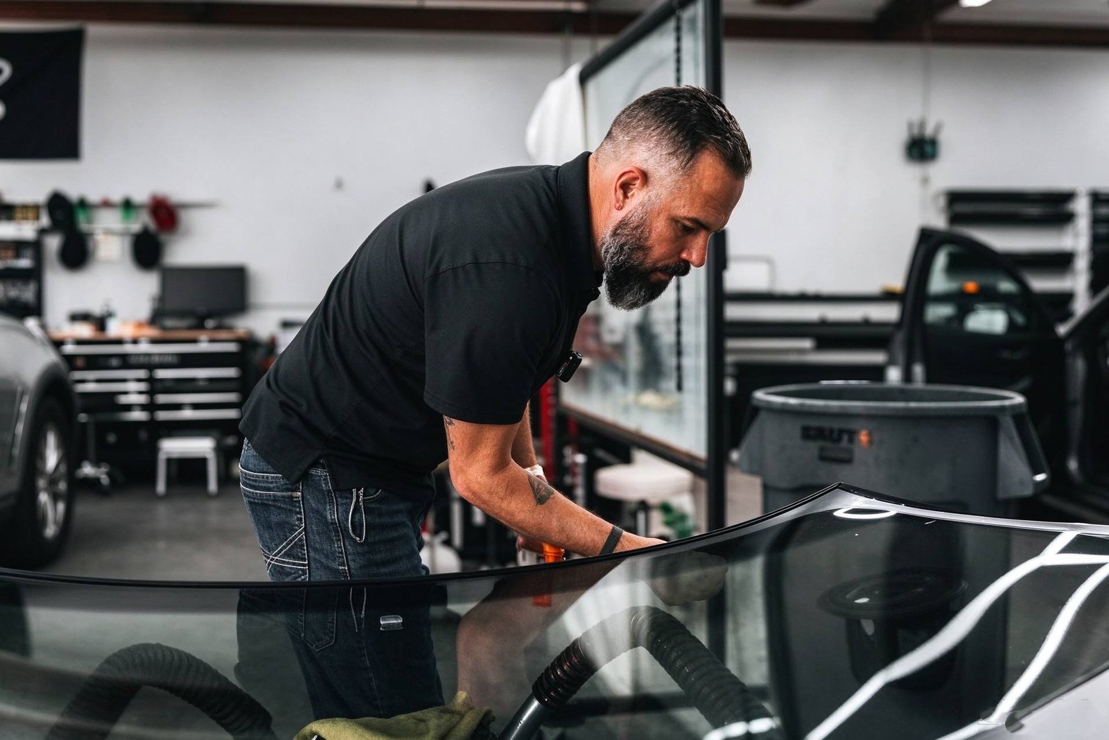 Technician extruding a precise triangular bead of polyurethane windshield adhesive onto the glass perimeter