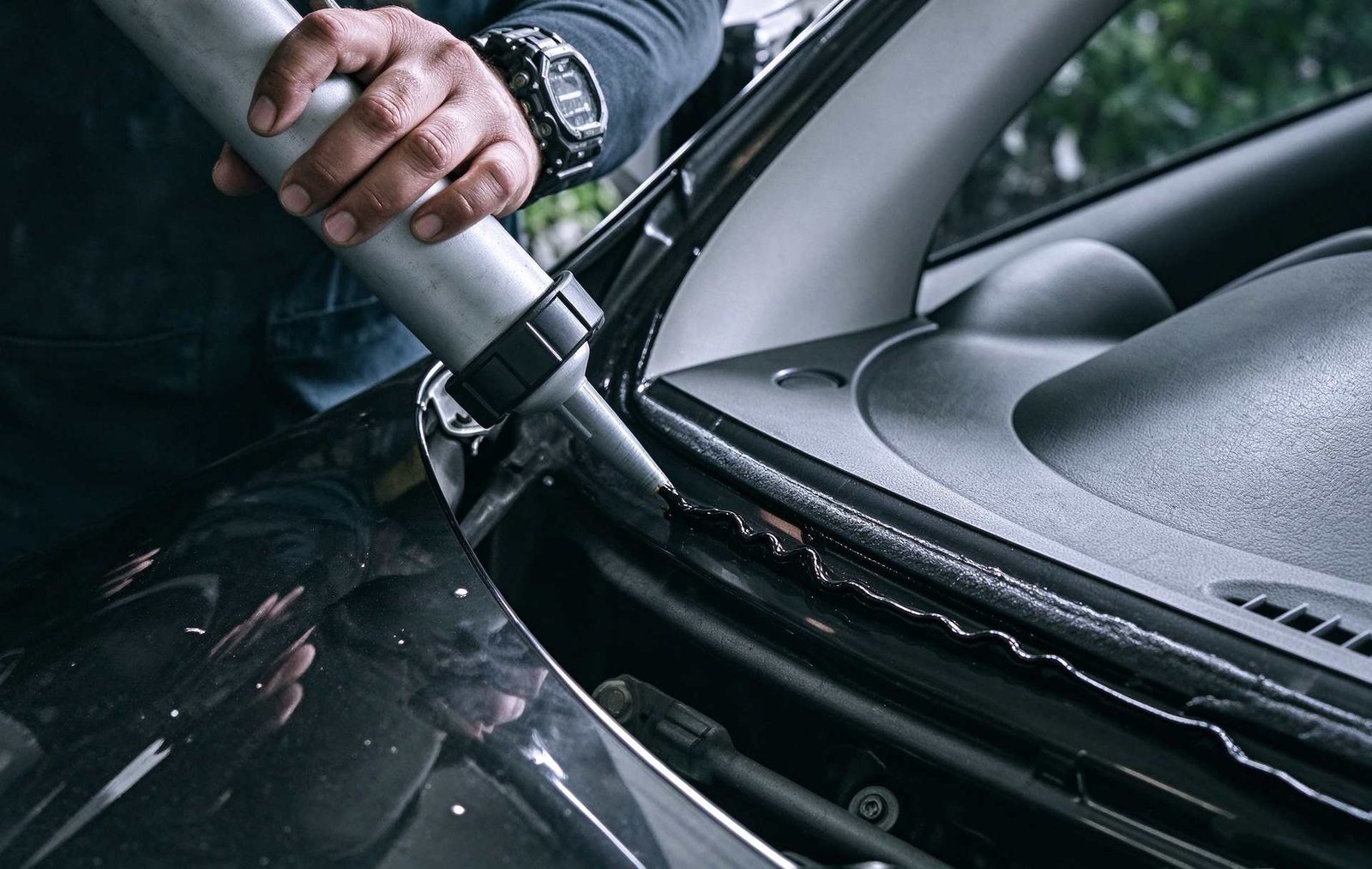 Technician carefully extruding adhesive along automotive glass edge to eliminate voids and guarantee water tightness