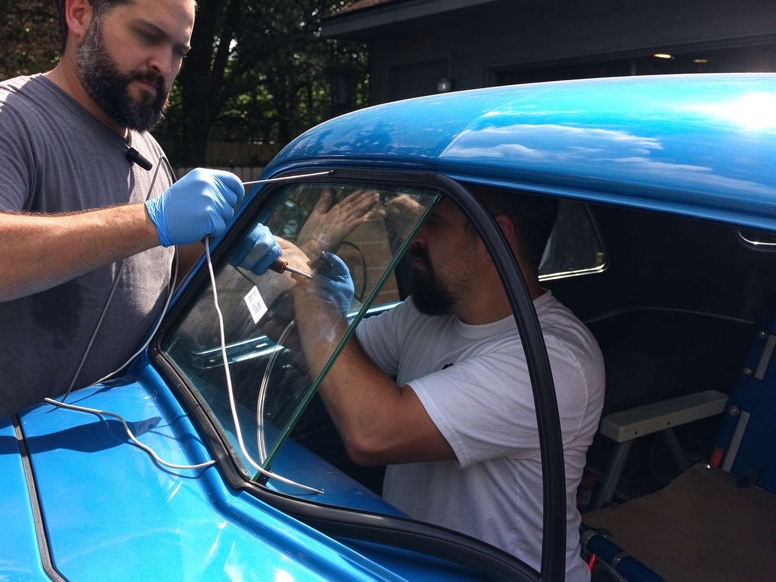 Two certified auto glass technicians lowering windshield into vehicle frame using professional vacuum suction lifters