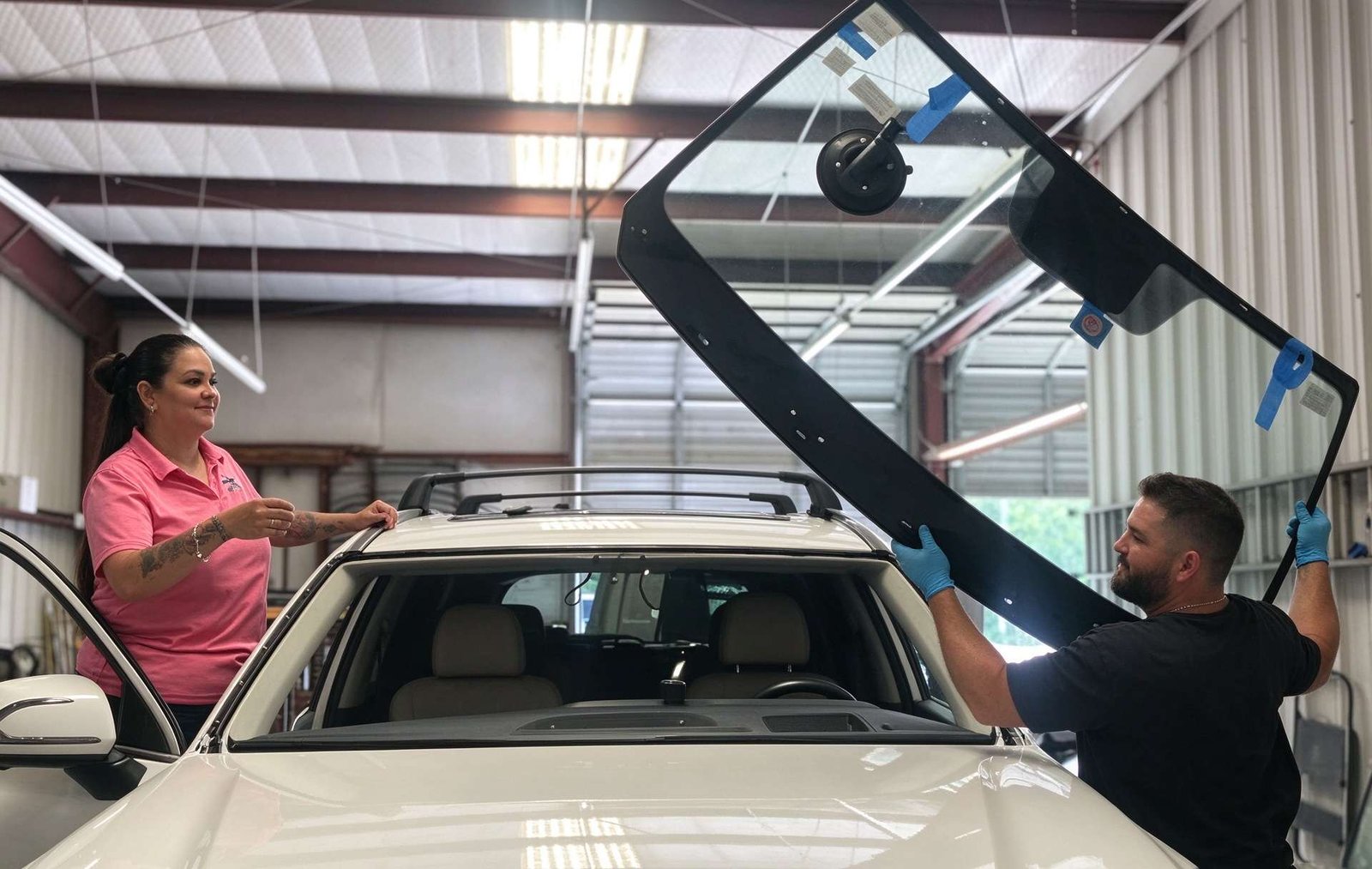 Two certified auto glass technicians carefully setting replacement windshield with precision alignment lifters