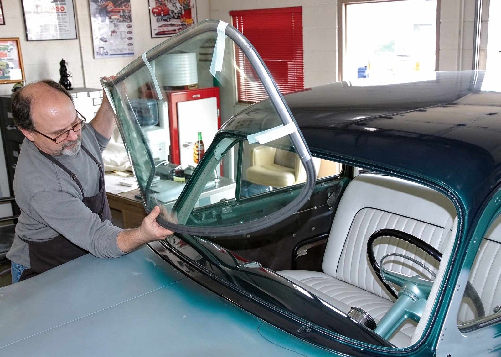 Two technicians carefully aligning and seating a replacement windshield onto prepared vehicle pinchweld