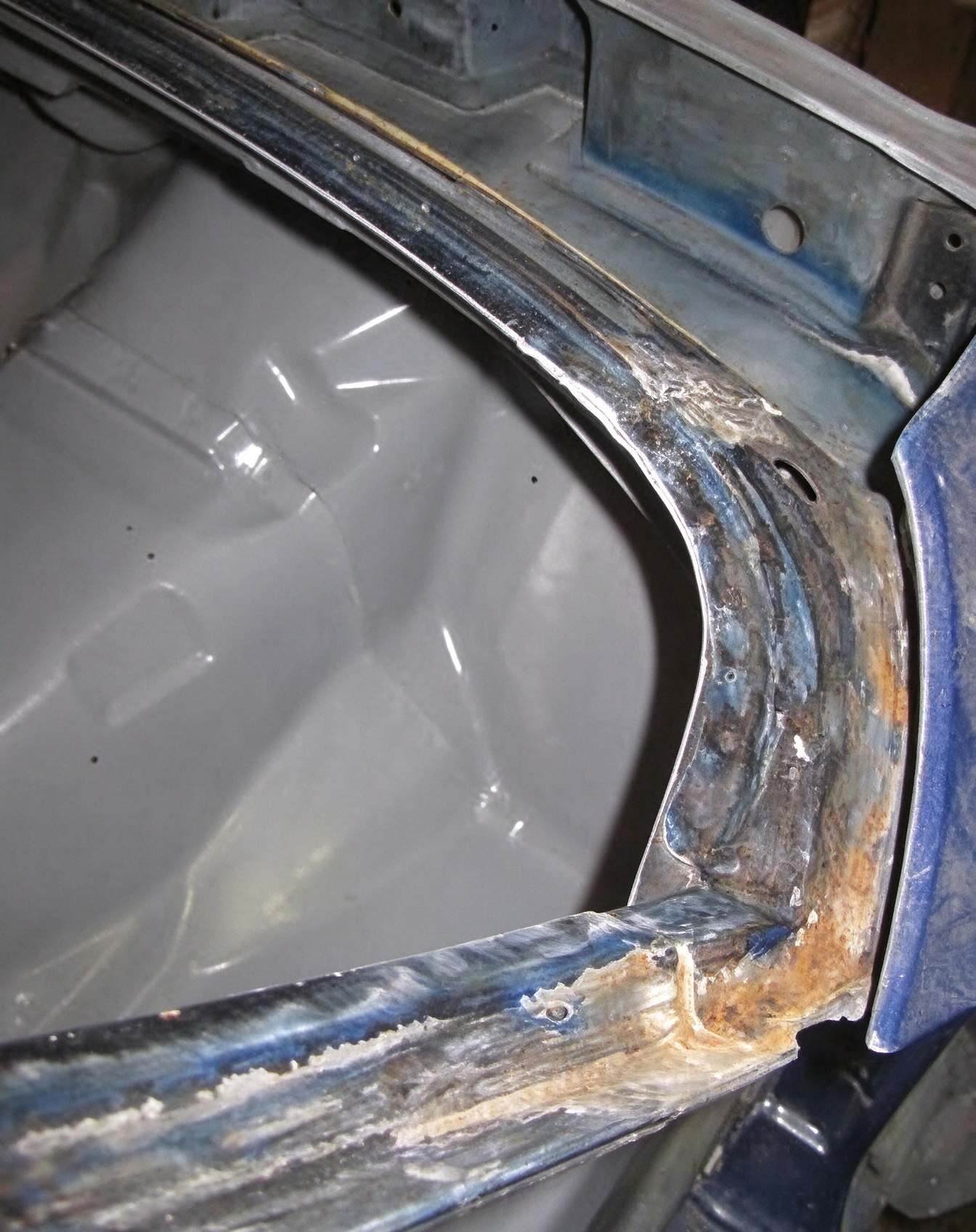 Body shop technician preparing vehicle frame mating flange and removing old adhesive residue for panel bonding