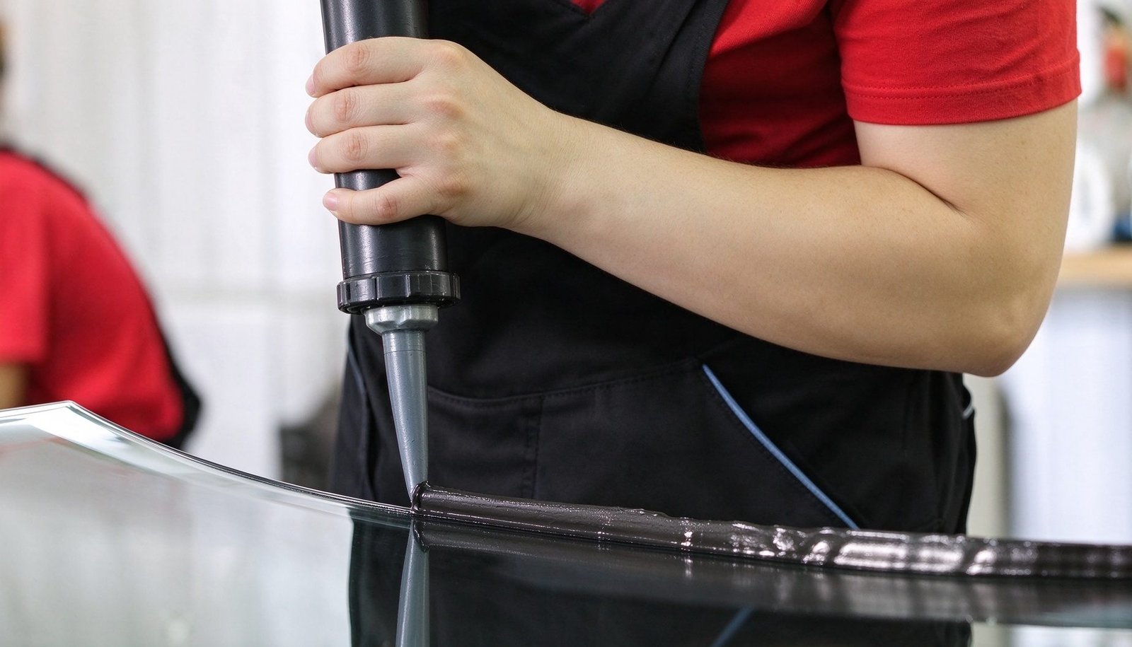 Automotive technician applying polyurethane direct glazing adhesive bead along car windshield frame aperture